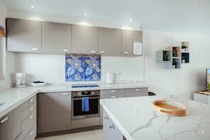 A modern kitchen with grey cabinets, a marble countertop, and a blue floral backsplash.