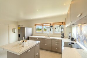 Une cuisine moderne dotée d’un grand îlot central, d’appareils électroménagers intégrés et offrant une vue sur l’extérieur.