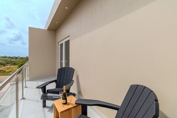 Un balcon avec deux chaises noires, une petite table en bois et une bouteille de champagne.
