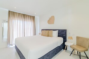 A modern hotel room with a large bed, a small side table, a chair, and a decorative wall piece.