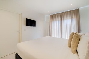 Une chambre à coucher avec un lit, un téléviseur fixé au mur et une fenêtre avec des rideaux.