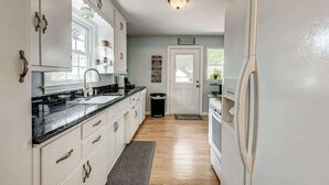 A kitchen with white cabinets, a black countertop, a white refrigerator, and a door leading to another room.