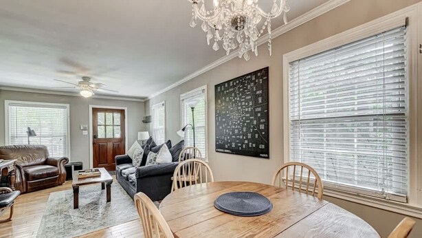 A living room with a wooden dining table, two sofas, a chandelier, and a large window with blinds.