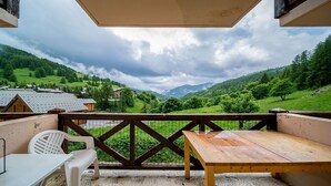 Un tavolo di legno e una sedia di plastica bianca su un balcone con vista su una valle verde e montagne.