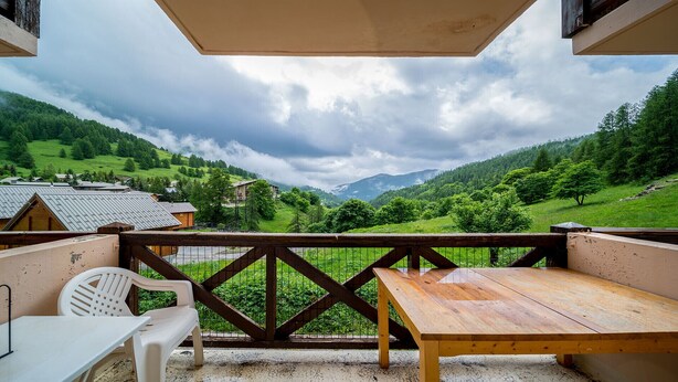 A wooden table and white plastic chair on a balcony with a view of a green valley and mountains. - Pleasant studio 4 ppl near the slopes (Allos)