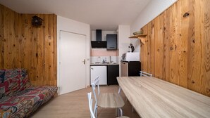 A compact living space with a wooden interior, a kitchenette, a dining area with a table and chairs, and a patterned sofa. - Pleasant studio 4 ppl near the slopes (Allos)