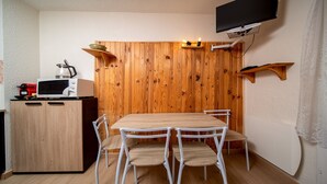 A compact kitchen with a wooden wall, a dining table with four chairs, a microwave, a kettle, and a TV mounted on the wall. - Pleasant studio 4 ppl near the slopes (Allos)