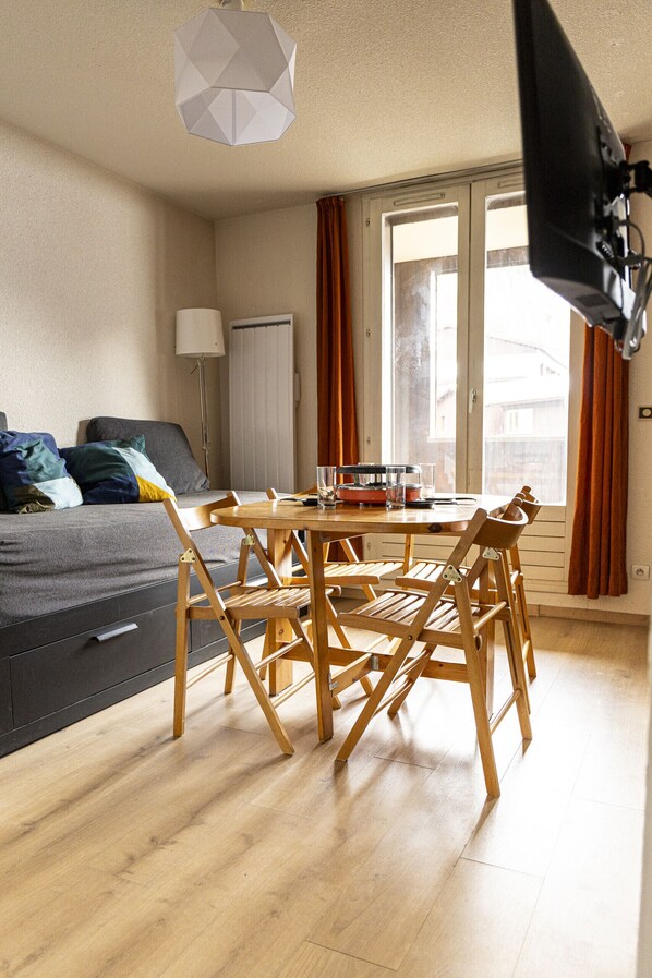 A room with a bed, a dining table with chairs, a lamp, and a window with curtains.