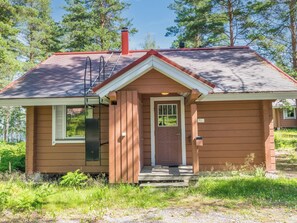A small, single-story wooden house with a red roof, a front door, and a small porch.