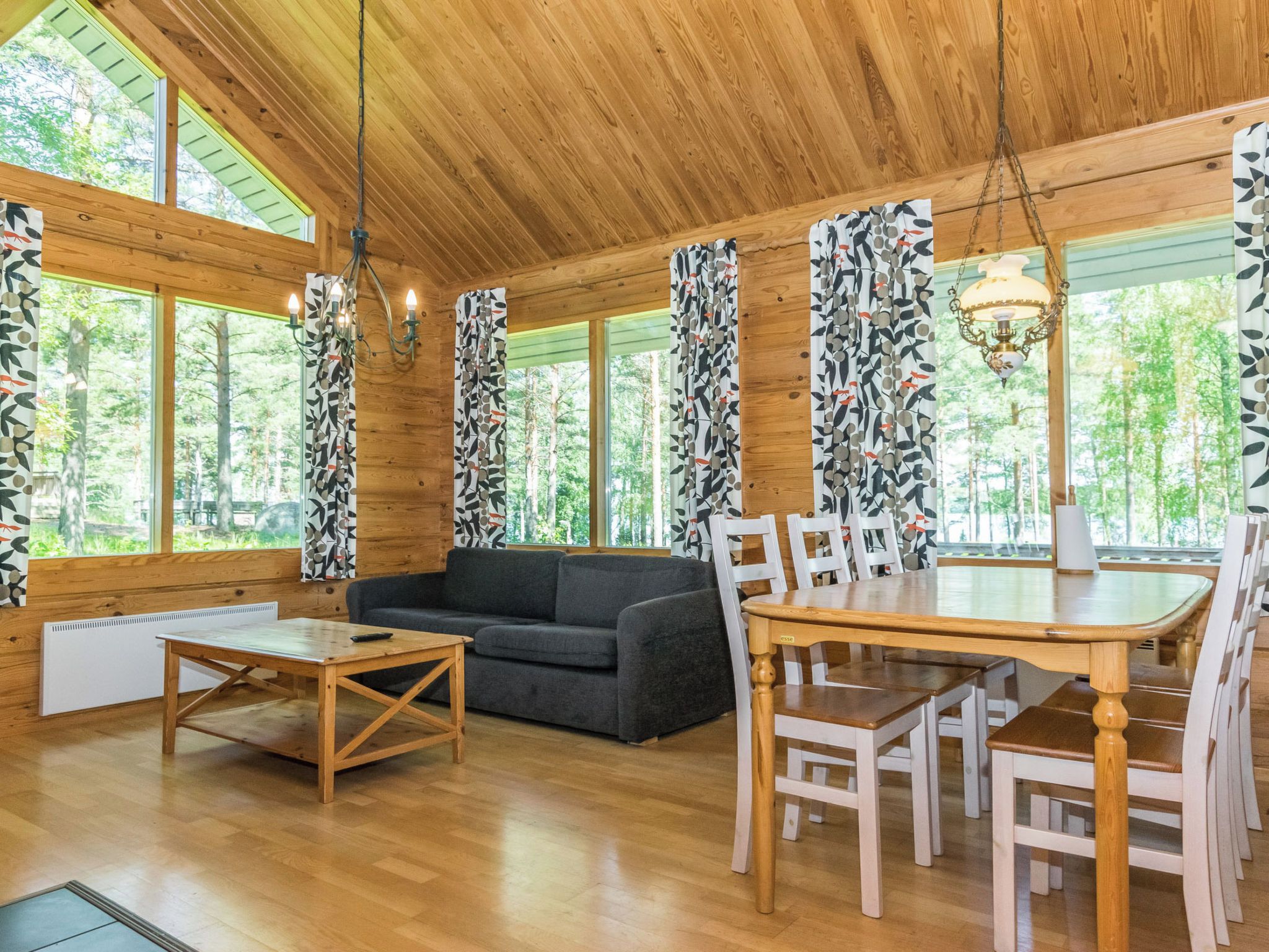 A wooden interior with a sofa, dining table, chairs, and large windows.