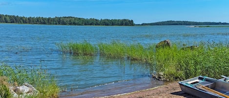 A calm lake with a boat docked on the shore, surrounded by greenery and trees.