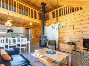 Interior acogedor de una cabaña con comedor, sofá, mesa, chimenea y televisor.