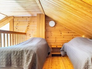 Une cabane avec deux lits, des murs en bois, un plafond en pente et une fenêtre bien visible.