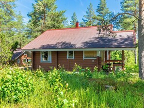 Une maison en bois avec un toit rouge, entourée de verdure et d’arbres.