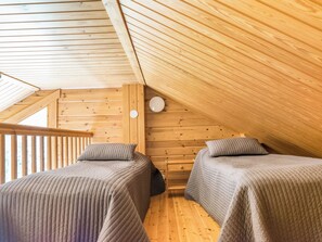 Een kleine, gezellige kamer onder de dakpannen met twee eenpersoonsbedden, houten wanden en een schuine hemel.