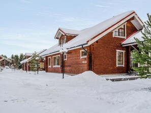 Una cabaña de madera con techo inclinado, rodeada de nieve.