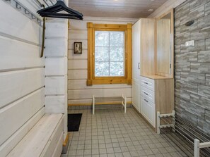 Un baño con ventana de madera, muebles blancos, un banco y suelo de baldosas.