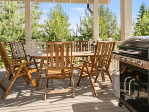 An outdoor patio with a wooden table and chairs, a grill, and a white fence.