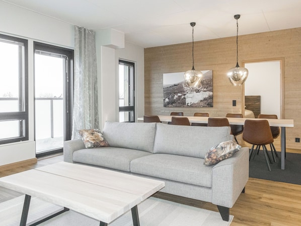 A modern living room with a sofa, a coffee table, and a dining area with chairs and a table.