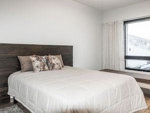 Un dormitorio con una cama grande, cabecera de madera y ventana con vistas a un paisaje nevado.