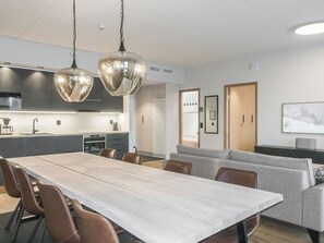 Ein moderner Essbereich mit einem langen Tisch und Stühlen, im Hintergrund eine Küche und eine Sitzecke mit einer Couch.