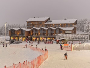 A multi-story lodge with a ski slope in front, featuring a snow-covered roof and wooden exterior.