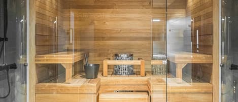 Una sauna con panche in legno e un tavolo centrale, pareti in vetro e pavimento piastrellato.