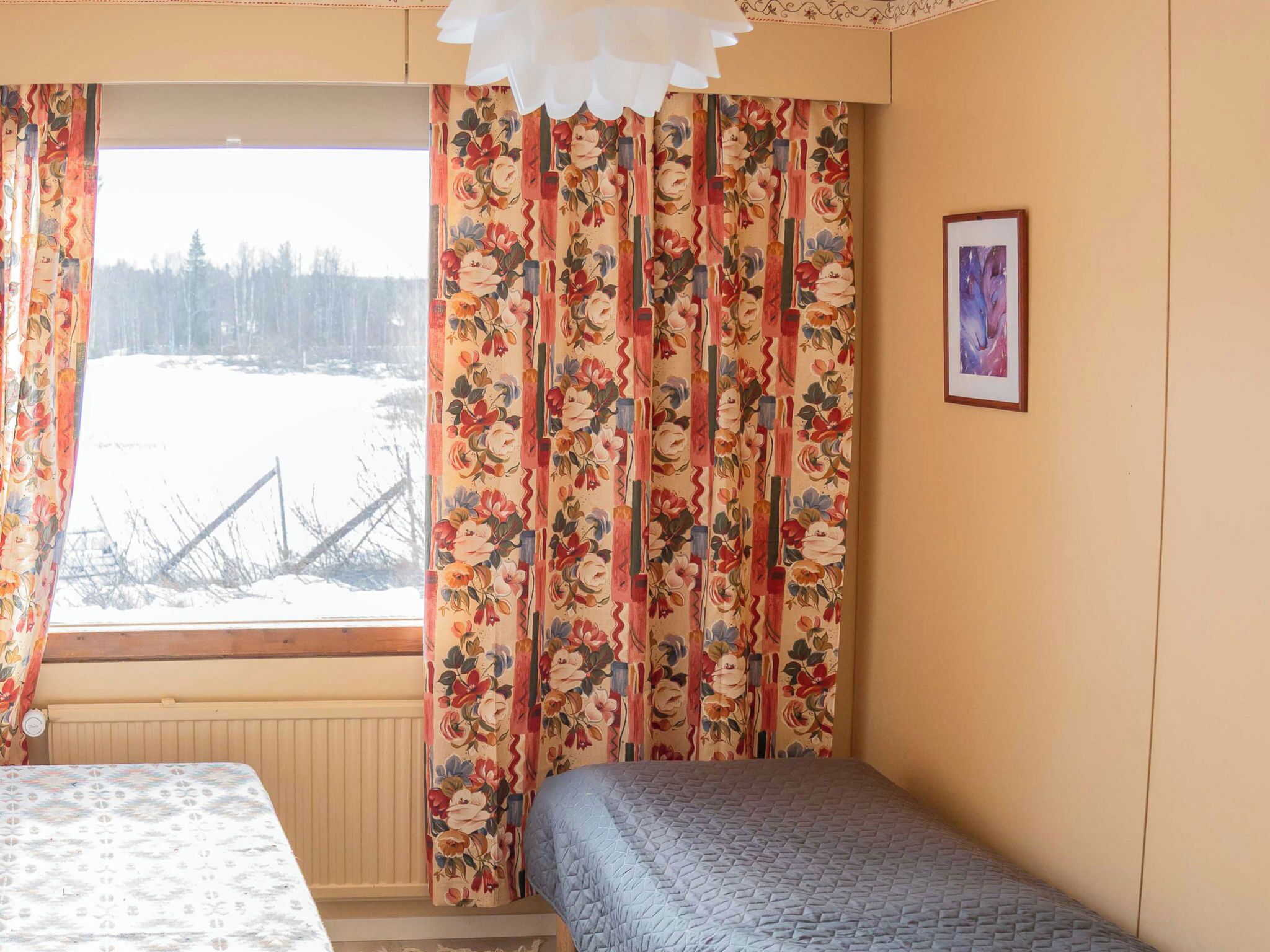 Ein Zimmer mit einem Bett, einem Vorhangfenster, einem Heizkörper und einem gerahmten Bild an der Wand.