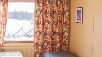 Ein Zimmer mit einem Bett, einem Vorhangfenster, einem Heizkörper und einem gerahmten Bild an der Wand.