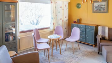 Uma sala de estar acolhedora com área de jantar, um aparador com portas de vidro, uma janela com cortinas e um quadro na parede.