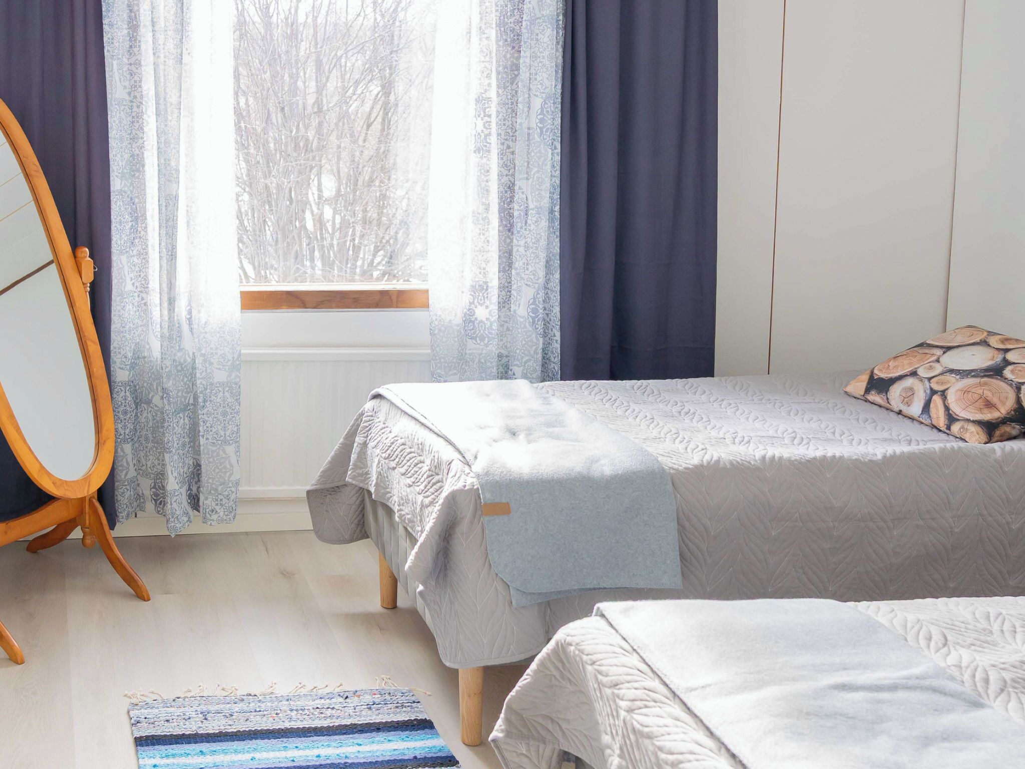 A bedroom with a bed, a wooden chair, a window with curtains, and a patterned rug.