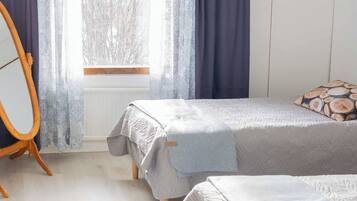 A bedroom with a bed, a wooden chair, a window with curtains, and a patterned rug.