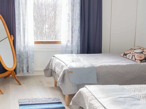 Makuuhuoneessa on sänky, puinen tuoli, ikkuna, jossa on verhot, ja kuviollinen matto.