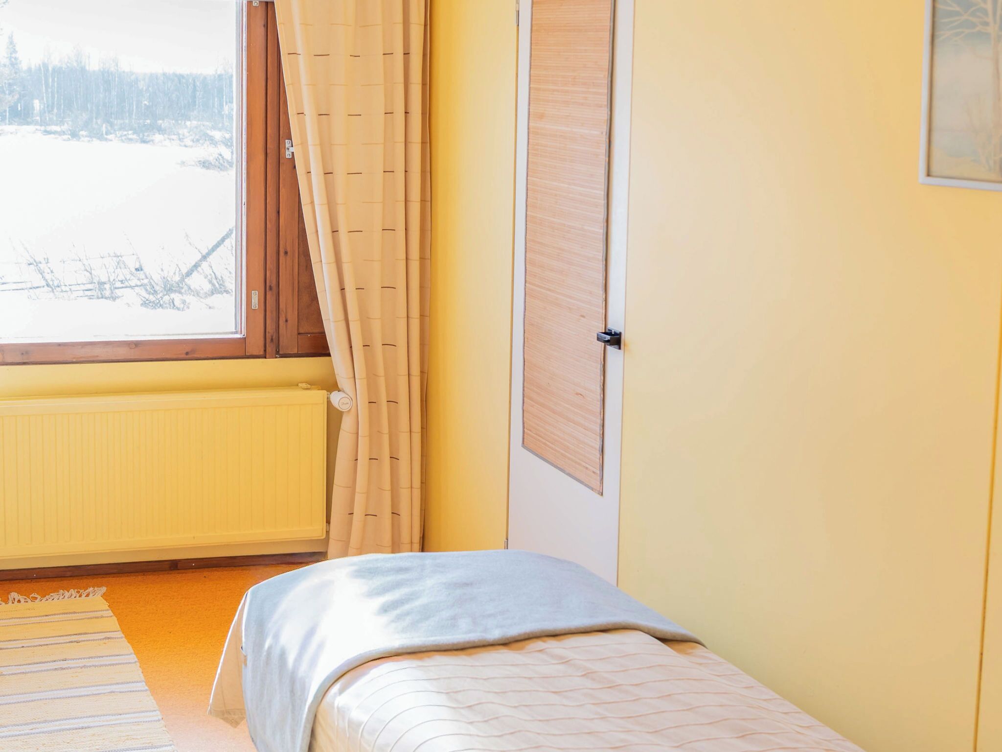 Ein Zimmer mit einem Bett, einem Vorhangfenster, einem Heizkörper und einer Tür.
