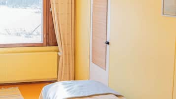 Ein Zimmer mit einem Bett, einem Vorhangfenster, einem Heizkörper und einer Tür.