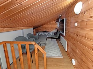 A cozy attic room with a wooden ceiling, a sofa set, a small table, and a TV mounted on the wall. - Pohjaslahdentie 17 a by Interhome (Kuusamo)