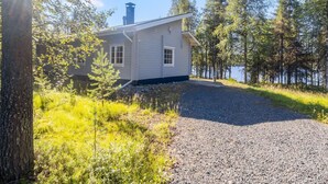 Une petite cabane à un seul étage, dotée d’une cheminée, entourée d’arbres et bordée d’une allée en gravier.