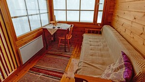 L’intérieur chaleureux d’un chalet avec un plancher en bois, un canapé recouvert d’une couverture tricotée, une table avec une nappe et de grandes fenêtres ornées de rideaux.