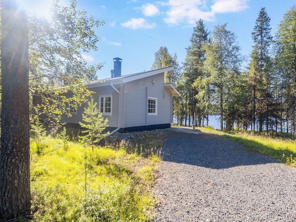 A house with a gravel driveway, surrounded by trees and a body of water.