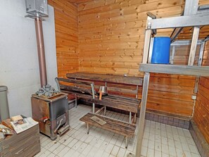 A sauna room with wooden walls, a bench, a heater, and a metal container with stones. - Pohjaslahdentie 17 a by Interhome (Kuusamo)