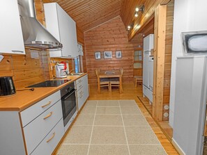 A compact kitchen with a wooden ceiling, a dining area with a table and chairs, and a refrigerator. - Pohjaslahdentie 17 a by Interhome (Kuusamo)