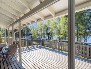 A covered deck with a view of a lake and trees, wooden furniture, and a wooden fence. - Pohjaslahdentie 17 b by Interhome (Kuusamo)