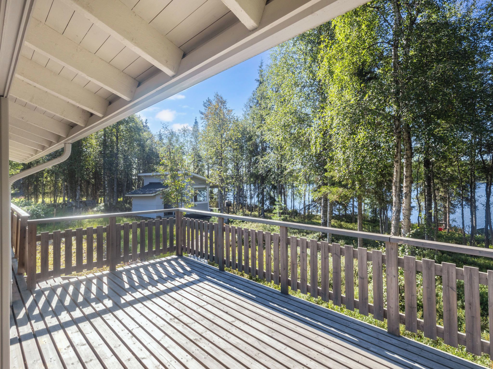 A wooden deck with a railing, overlooking a forested area and a body of water.