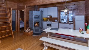 A cozy cabin interior with a wood-burning stove, a dining table, and a bench. - Pohjaslahdentie 17 b by Interhome (Kuusamo)