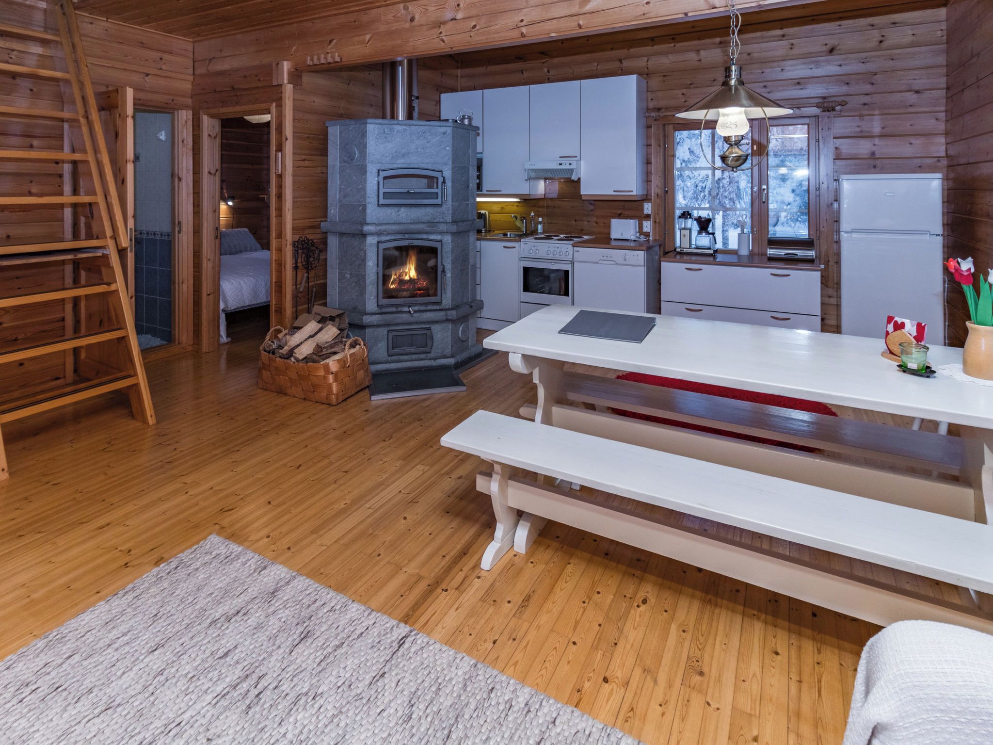 L’intérieur chaleureux d’un chalet avec une cheminée en pierre, un plancher en bois, une table à manger et un coin cuisine.