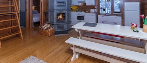 L’intérieur chaleureux d’un chalet avec une cheminée en pierre, un plancher en bois, une table à manger et un coin cuisine.
