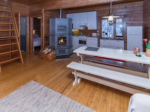 A cozy cabin interior with a stone fireplace, wooden floors, a dining table, and a kitchen area. - Pohjaslahdentie 17 b by Interhome (Kuusamo)