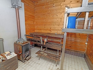 A sauna room with wooden walls, a bench, a heater, and a metal container with stones. - Pohjaslahdentie 17 b by Interhome (Kuusamo)