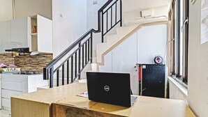 A room with a wooden desk, a laptop, a chair, a staircase, and a kitchen area. - OYO LIFE 93634 Penginapan D'palinggihan Syariah (Sumber)