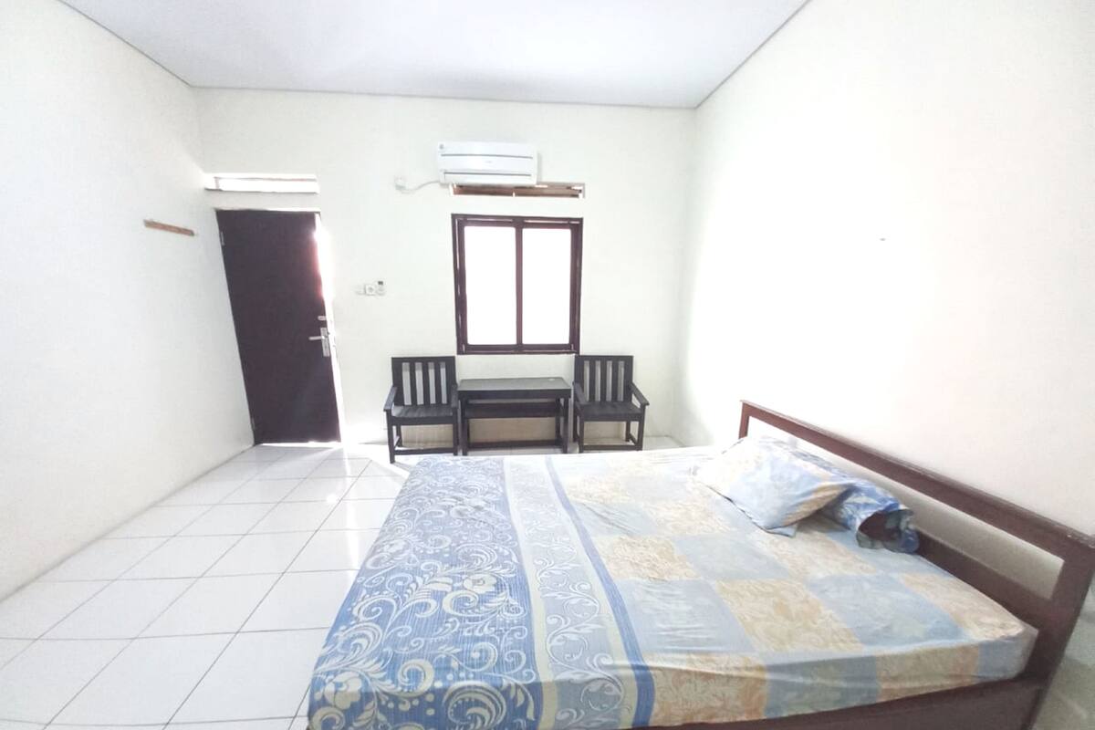 A bedroom with a bed, two chairs, a window, and an air conditioner.